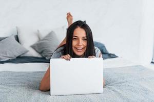 junge schöne frau in lässiger kleidung, die sich allein zu hause mit laptop hinlegt foto