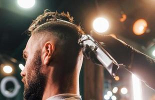 Nahaufnahme eines jungen bärtigen Mannes, der im Friseursalon sitzt und sich die Haare schneiden lässt foto