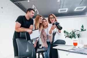 Gruppe von Geschäftsleuten in formeller Kleidung drinnen im Büro, die Fotos auf der Kamera betrachten