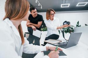 Gruppe von Geschäftsleuten in formeller Kleidung drinnen im Büro, die Fotos auf der Kamera betrachten