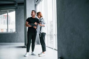 Frau in formeller Kleidung und mit Kamera in der Hand, die mit einem Mann in einem leeren Raum steht foto