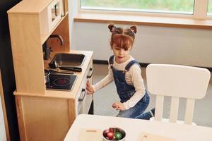 Kleines Mädchen in Freizeitkleidung hat Spaß beim Spielen mit Spielzeug in der Küche foto