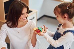 junge frau mit kleinem mädchen, das zusammen mit spielzeug in der küche spielt foto