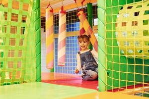 glückliches kleines mädchen in lässiger kleidung hat spaß im kinderspielkomplex foto