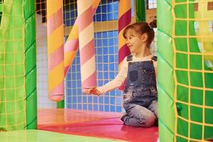 glückliches kleines mädchen in lässiger kleidung hat spaß im kinderspielkomplex foto