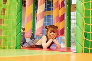 glückliches kleines mädchen in lässiger kleidung hat spaß im kinderspielkomplex foto