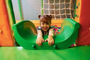 glückliches kleines mädchen in lässiger kleidung hat spaß im kinderspielkomplex foto