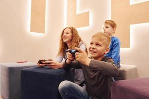 Fröhliche Kinder, die drinnen sitzen und zusammen Videospiele spielen foto