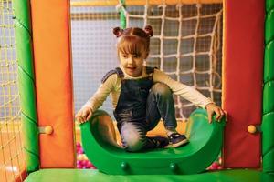 glückliches kleines mädchen in lässiger kleidung hat spaß im kinderspielkomplex foto