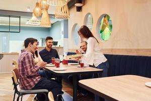 Gruppe junger Freunde, die drinnen zusammensitzen und Pizza essen foto