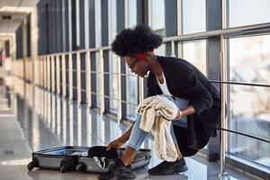 junge afroamerikanische passagierin in freizeitkleidung ist am flughafen mit gepäckverpackungskleidung foto