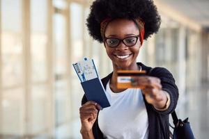 junge afroamerikanische passagierin in lässiger kleidung ist am flughafen und hält tickets und kreditkarte foto