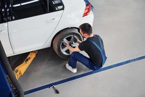 Mann in Arbeitsuniform sitzt und wechselt drinnen das Autorad. Konzept des Autoservices foto