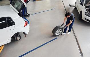 Ansicht von oben. Mann in Arbeitsuniform, der drinnen mit dem Autorad läuft. Konzept des Autoservices foto