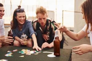 Kartenspiel spielen. eine gruppe junger leute in lässiger kleidung feiert tagsüber zusammen eine party auf dem dach foto