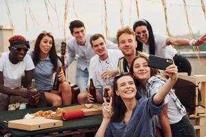 Mädchen macht Selfie. mit leckerer Pizza. eine gruppe junger leute in lässiger kleidung feiert tagsüber zusammen eine party auf dem dach foto