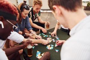 Kartenspiel spielen. eine gruppe junger leute in lässiger kleidung feiert tagsüber zusammen eine party auf dem dach foto