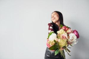 schöne junge Brünette im schwarzen Rock, die drinnen vor weißem Hintergrund steht, mit Blumenstrauß in den Händen foto