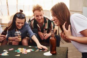 Kartenspiel spielen. eine gruppe junger leute in lässiger kleidung feiert tagsüber zusammen eine party auf dem dach foto