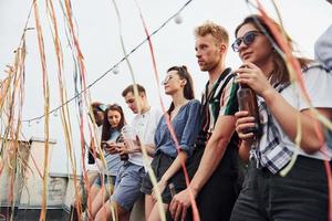 an den Rand des Daches gelehnt mit Dekorationen. Gruppe junger Leute in Freizeitkleidung feiern tagsüber zusammen foto