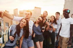 Selfies machen. schöner Sonnenschein. eine gruppe junger leute in lässiger kleidung feiert tagsüber zusammen eine party auf dem dach foto