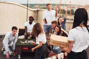 leckere Pizzen. eine gruppe junger leute in lässiger kleidung feiert tagsüber zusammen eine party auf dem dach foto