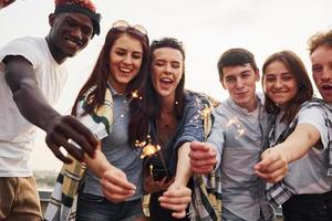 mit Wunderkerzen in den Händen. eine gruppe junger leute in lässiger kleidung feiert tagsüber zusammen eine party auf dem dach foto