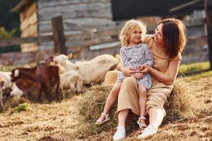 junge mutter mit ihrer tochter ist im sommer mit ziegen auf dem bauernhof foto