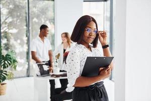 schöne Frau mit Brille vor ihren Kollegen. gruppe afroamerikanischer geschäftsleute, die gemeinsam im büro arbeiten foto