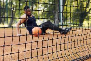 müder afroamerikaner sitzt mit ball auf dem platz im freien auf dem boden. macht eine Pause foto