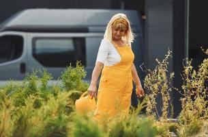 Seniorin in gelber Uniform ist tagsüber im Garten und gießt Pflanzen foto