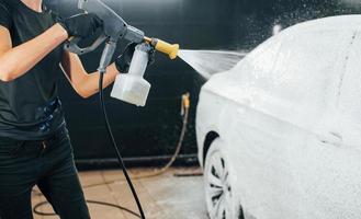 unter Verwendung von Hochdruckwasser. Modernes schwarzes Auto wird von einer Frau in der Autowaschanlage gereinigt foto