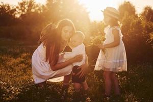 fröhliche familie von mutter, kleinem sohn und tochter, die an sonnigen sommertagen freizeit auf dem feld verbringen foto