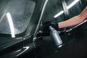Besprühen des Fahrzeugs. Modernes schwarzes Auto wird von einer Frau in der Autowaschanlage gereinigt foto
