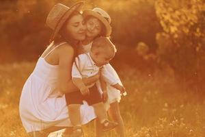 glückliche familie von mutter, kleinem sohn und tochter, die an sonnigen sommertagen freizeit auf dem feld verbringen foto