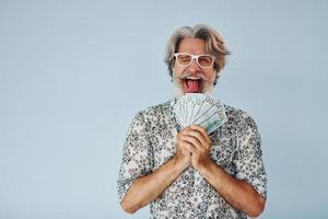 Millionär mit Bargeld in den Händen. Senior stilvoller moderner Mann mit grauem Haar und Bart drinnen foto