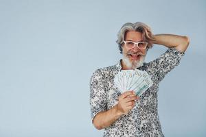 Millionär mit Bargeld in den Händen. Senior stilvoller moderner Mann mit grauem Haar und Bart drinnen foto