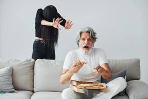 Fernsehen mit gruseliger Frau mit schwarzen Haaren in seiner Nähe. älterer stilvoller moderner mann mit grauem haar und bart zuhause foto