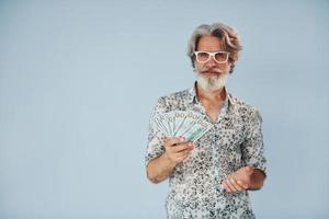 Millionär mit Bargeld in den Händen. Senior stilvoller moderner Mann mit grauem Haar und Bart drinnen foto