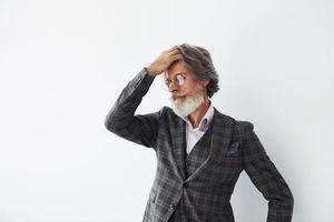 posiert für eine Kamera im Stehen vor weißem Hintergrund. älterer stilvoller moderner mann mit grauem haar und bart zuhause foto