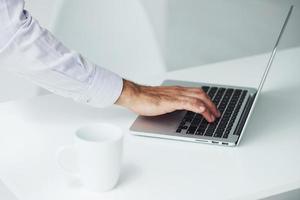 Nahaufnahme der Hand des Mannes, die im Büro auf dem Laptop tippt foto