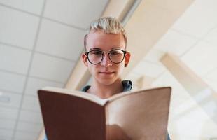 junger männlicher College-Student mit Brille, der drinnen Buch liest