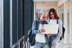 Zwei junge Studentenfreunde zusammen in einem Korridor eines Colleges mit Laptop in den Händen foto