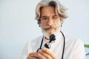 Das Porträt eines leitenden männlichen Arztes mit grauem Haar und Bart im weißen Mantel befindet sich in der Klinik für Hals-Nasen-Ohrenheilkunde foto