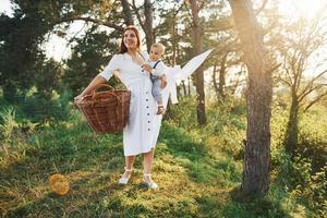 positive hausfrau mit hängt weiße kleidung zum trocknen. junge mutter mit ihrem kleinen sohn ist draußen im wald. schöner Sonnenschein foto