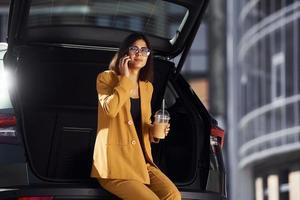 Gespräche per Telefon. junge modische frau in burgunderfarbenem mantel tagsüber mit ihrem auto foto