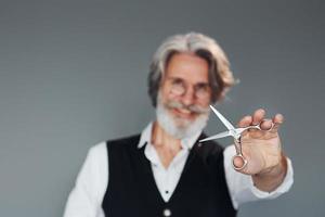 Friseurwerkzeuge. vor grauem Hintergrund. Stilvoller moderner Senior mit grauem Haar und Bart ist drinnen foto