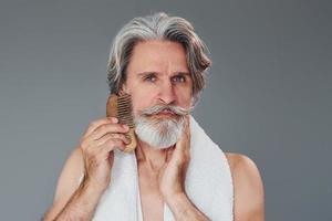 Pflege von Gesicht und Hautreinheit. Stilvoller moderner Senior mit grauem Haar und Bart ist drinnen foto