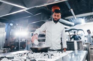 verwendet Bratpfanne. Koch in weißer Uniform, der Essen in der Küche kocht. arbeitsreicher Tag foto