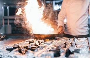 Bratpfanne brennt. Koch in weißer Uniform, der Essen in der Küche kocht. arbeitsreicher Tag foto